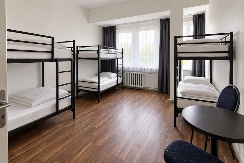 KI-Visualisierung eines Sechser-Hostelzimmers mit drei Etagenbetten und Sitzplatz am Fenster